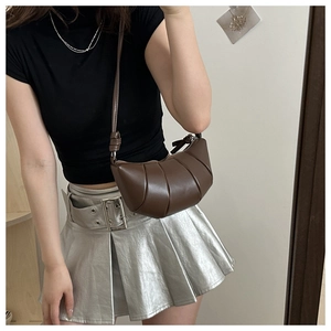 Detail of a dark brown leather croissant bag with pleated texture on female shoulder
