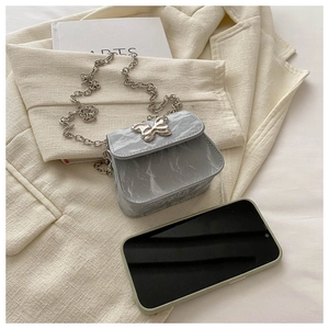 Mini sac à bandoulière marbré avec fermoir papillon présenté à côté d'un smartphone
