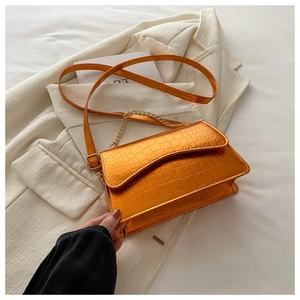 Detail of orange crocodile pattern embossed leather bag with gold chain and flap closure