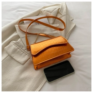 Detail of metallic orange crocodile embossed bag with chain strap and phone for scale