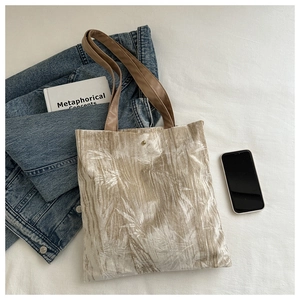 Close-up of beige velvet tote bag with silver bamboo pattern and brown leather handles