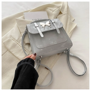 Detail of vintage grey crossbody bag featuring a metal butterfly and cracked texture