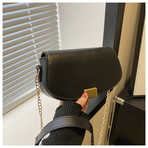 Close-up of black saddle bag featuring gold striped metal lock and chain strap detail
