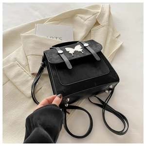 Detail of black crossbody bag with silver butterfly charm on a white blazer