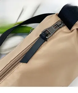 Detailed view of gunmetal zipper and black puller on a beige nylon crossbody bag