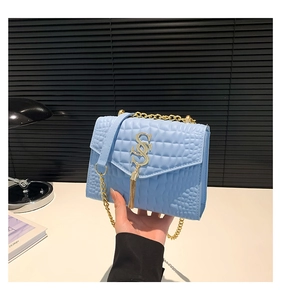 Détail d'un sac bandoulière bleu clair avec texture croco et bandoulière en chaîne dorée
