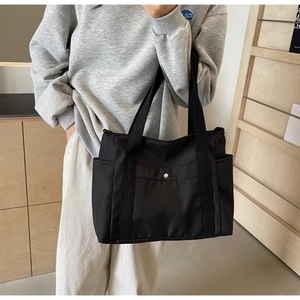 Detail of a black nylon tote bag featuring a front metal snap pocket and side pouches