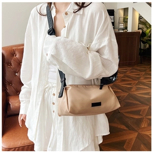 Close-up of beige nylon crossbody bag with black adjustable strap worn by a model