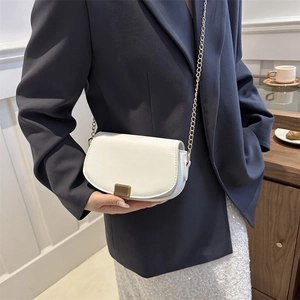 Elegant white faux leather saddle bag with gold chain strap shown in a lifestyle setting