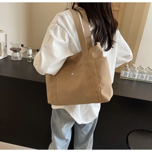 Detail of light brown nylon tote bag featuring a front pocket and wide shoulder strap