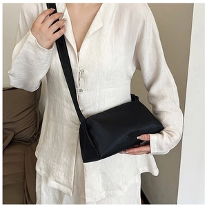 Detail of black crossbody pillow bag with wide textured letter strap on casual outfit