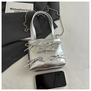 Silver mini tote bag with bow details next to a smartphone showing compact size