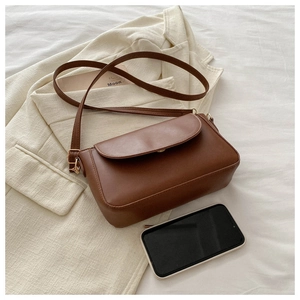 Detail shot of a retro brown leather crossbody bag with a gold buckle on a white blazer