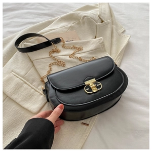 Detail of black saddle bag featuring gold buckle and chain strap on white blazer