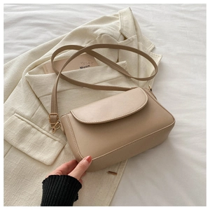 Detail of beige crossbody bag with curved flap, gold buckle on stylish blazer background