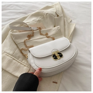 Detail of white saddle bag with vintage gold buckle and chain strap on beige blazer
