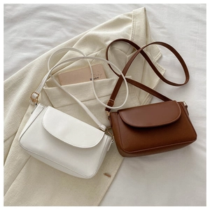 Flat lay of vintage beige and caramel leather crossbody bags on a cream blazer backdrop