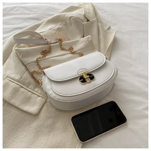 Detail of white saddle bag with black-gold oval clasp and chain strap on fabric background