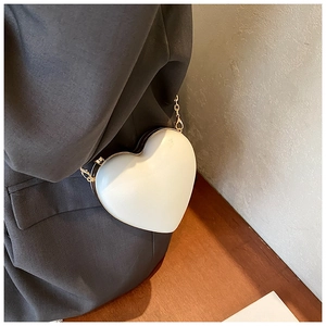 Detail der weißen herzförmigen Umhängetasche mit goldener Kette auf einem grauen Blazer