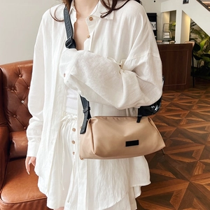 Minimalist beige dumpling crossbody bag with wide black strap on a vintage leather sofa