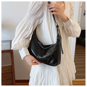 Glossy black crescent shoulder bag styled with a white dress for a minimalist look