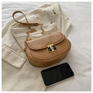 Caramel saddle bag with golden clasp shown next to a smartphone for size reference