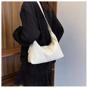 Close-up of beige glossy PU leather shoulder bag with pleated details on a model