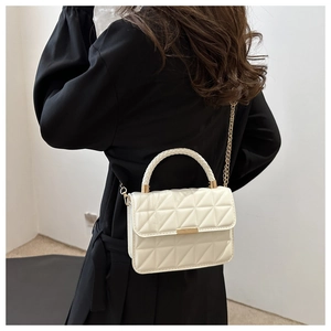 Detail of white quilted crossbody bag with gold chain and woven handle on black coat