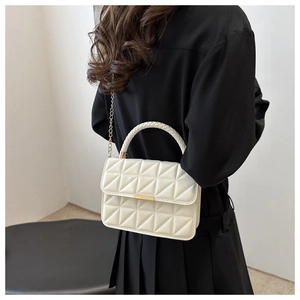 Detail of white quilted crossbody bag with gold buckle and woven handle craftsmanship