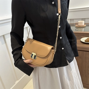 Chic tan saddle bag with gold chain strap and oval metallic buckle on a stylish model