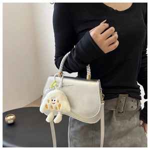 Detail of silver metallic saddle bag with woven handle and plush charm on a model