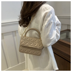 Close-up of beige quilted crossbody bag with gold chain and woven handle on model