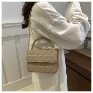 Detail of beige quilted crossbody bag with golden chain strap on a white linen shirt