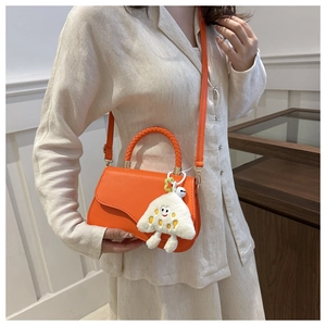 Detail of orange woven handle crossbody bag with a white plush mushroom charm on side
