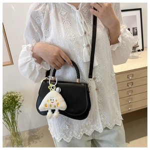 Detail of black saddle bag with woven handle and plush cloud charm in home setting