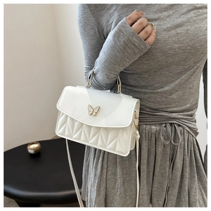 Close-up of white crossbody bag with golden butterfly buckle and quilted diamond pattern