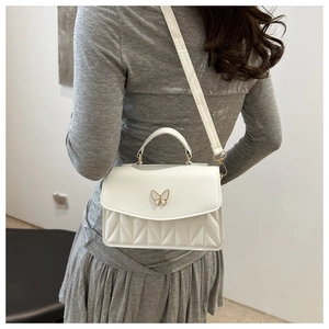 Detail of white PU leather crossbody bag featuring butterfly clasp and quilted pattern