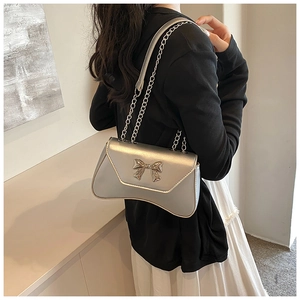 Detail of silver metallic shoulder bag featuring a 3D metal bow and fine chain strap