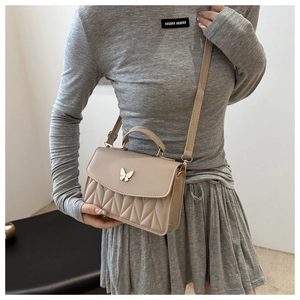Detail of beige quilted crossbody bag with metal butterfly and textured stitching