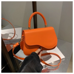 Detail of orange leather saddle bag with woven handle and wave flap design on a mirror surface