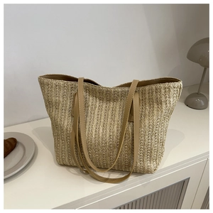 Detail of a large woven straw tote bag with brown leather straps in a home setting