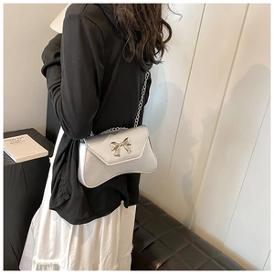 Silver shoulder bag with metal bow detail and chain strap worn by model in daily style