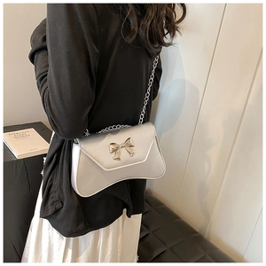 Silver-grey crossbody bag featuring a metal bow detail and elegant chain strap on a model