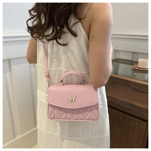 Pink crossbody bag featuring white butterfly ornament and quilted texture on white lace dress