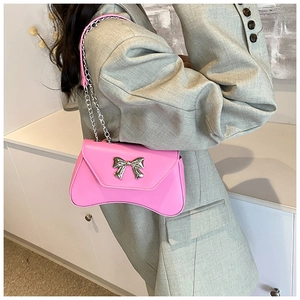 Detail of pink shoulder bag featuring silver metal bow and leather chain strap