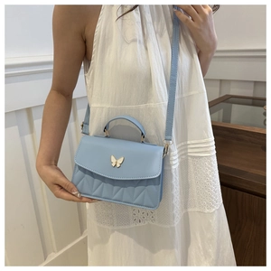 Close-up of elegant light blue crossbody bag with golden butterfly buckle and quilted texture