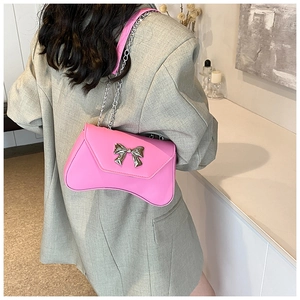 Pink underarm bag with silver bow buckle and curved bottom on grey suit model