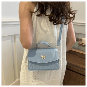 Close-up of a light blue crossbody bag with a butterfly clasp on a white lace dress