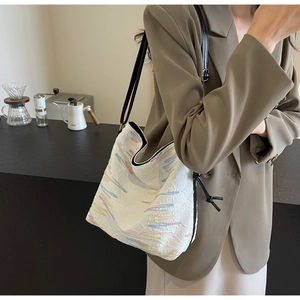 Détail d'un sac cabas blanc à rayures colorées avec cordon noir porté sur l'épaule de côté