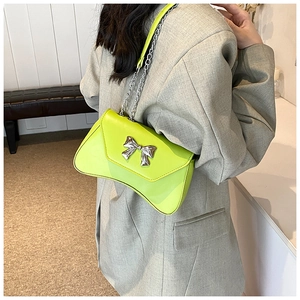 Close-up of lime green baguette bag with silver bow accent and chain strap on model